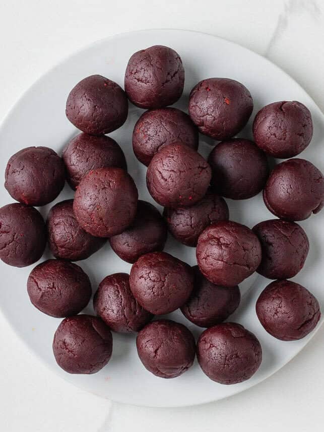 Grinch cake pops are made with moist red velvet cake and decorated with green candy coating and a little red heart. A festive Christmas dessert inspired by the classic movie! Plate of rolled cake balls before dipping, first step in making Christmas cake pops.