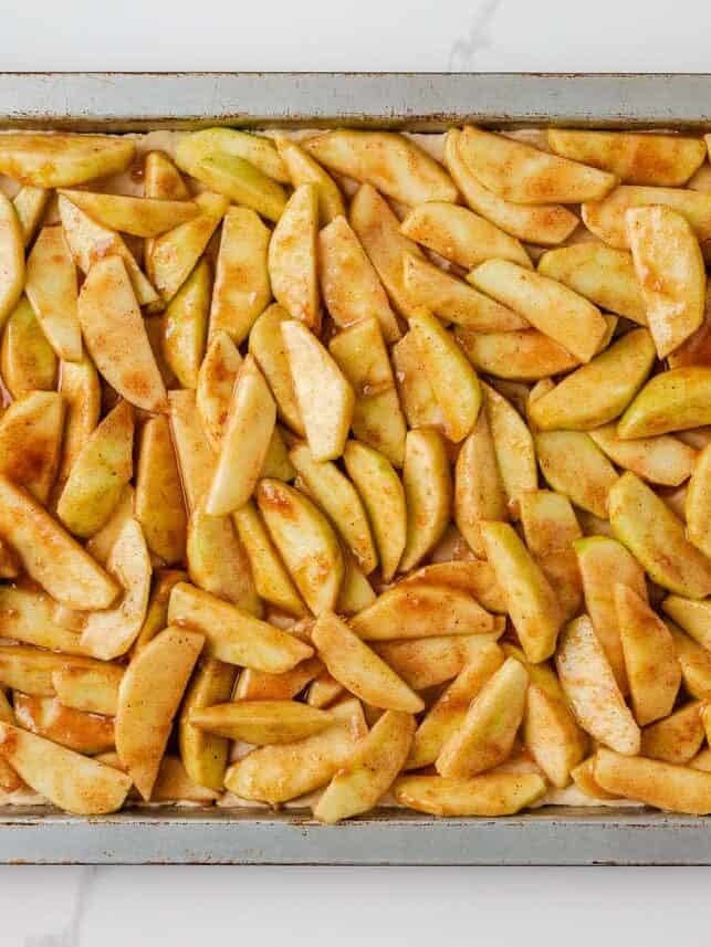 Rectangular pan filled with sliced apples tossed in cinnamon sugar for apple slab pie filling.