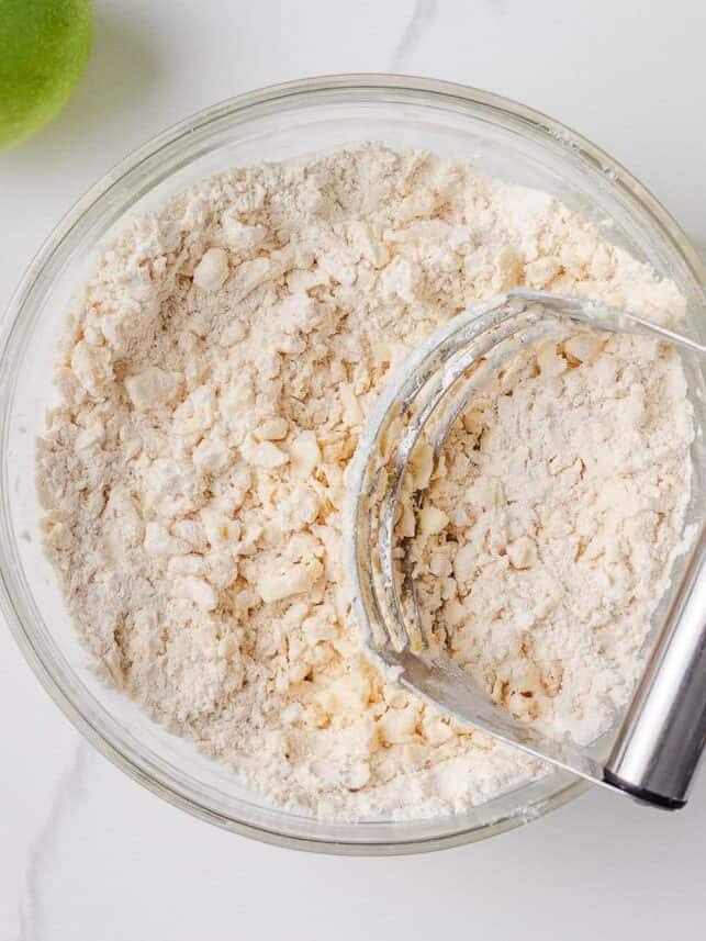 Bowl of flour and butter mixture being cut together with a pastry cutter for pie crust.