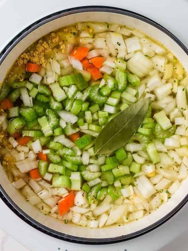 A creamy twist on a classic soup, this easy-to-make creamy chicken noodle soup is exactly what you need when you're curled up under a blanket this winter! Soup pot filled with onions, carrots, celery, seasonings, and a bay leaf before adding noodles and chicken.