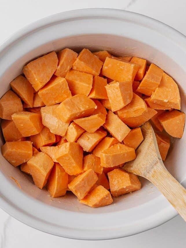 Crockpot sweet potato casserole makes holiday cooking easy. With creamy mashed sweet potatoes and a crunchy pecan topping, it's a holiday side dish not to be missed! Uncooked sweet potato chunks in crockpot before mashing for casserole.