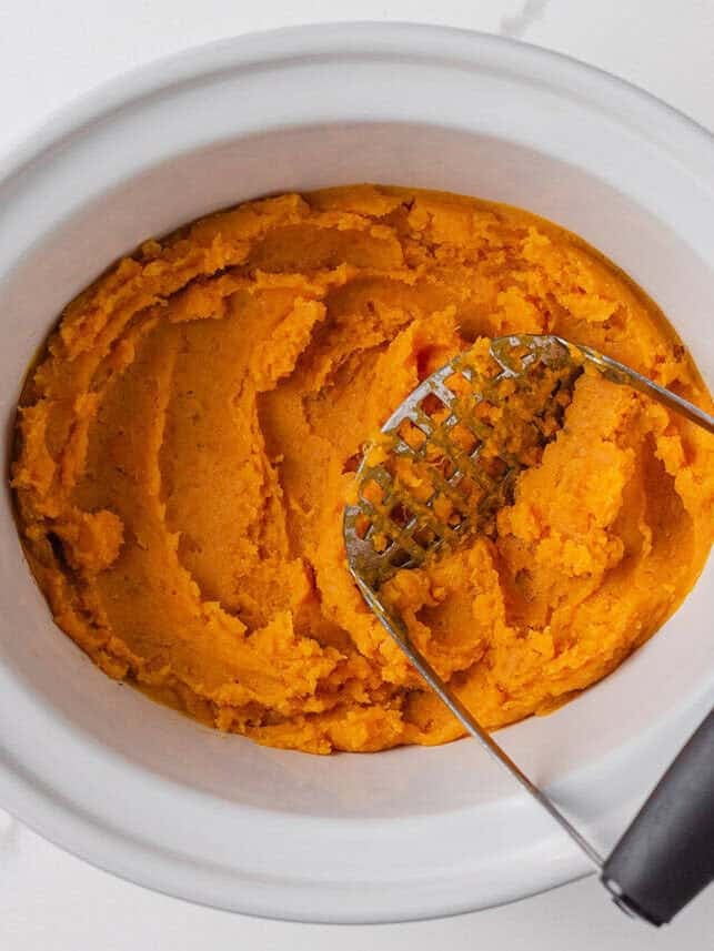 Crockpot sweet potato casserole makes holiday cooking easy. With creamy mashed sweet potatoes and a crunchy pecan topping, it's a holiday side dish not to be missed! Mashed sweet potatoes in slow cooker with potato masher.