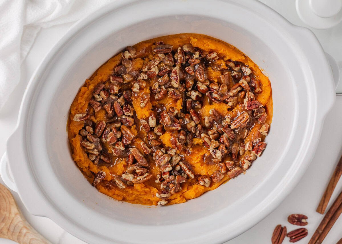 Crockpot sweet potato casserole makes holiday cooking easy. With creamy mashed sweet potatoes and a crunchy pecan topping, it's a holiday side dish not to be missed! Slow cooker sweet potato casserole with pecan topping ready to serve.