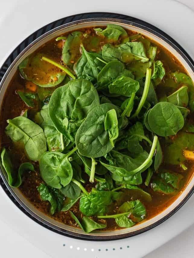 Fresh spinach added to the soup base before simmering.