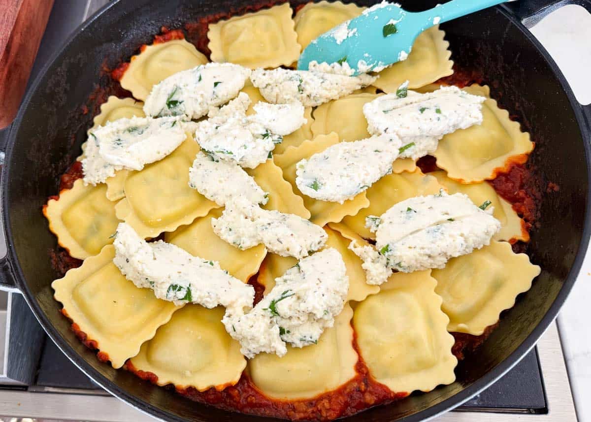 Frozen cheese ravioli in a skillet topped with dollops of ricotta and parsley cheese mixture.