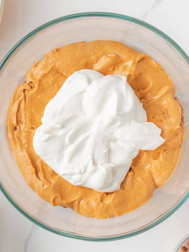 Whipped cream spooned over pumpkin cheesecake layer in the trifle before adding more cake and toppings.