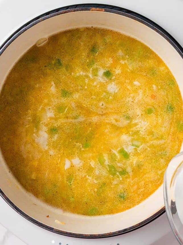 This creamy sausage potato soup is made in one pot with Italian sausage, tender potatoes, and a cheesy broth, it's a cozy way to satisfy the whole family! Simmering broth and adding in half and half to the Dutch oven.