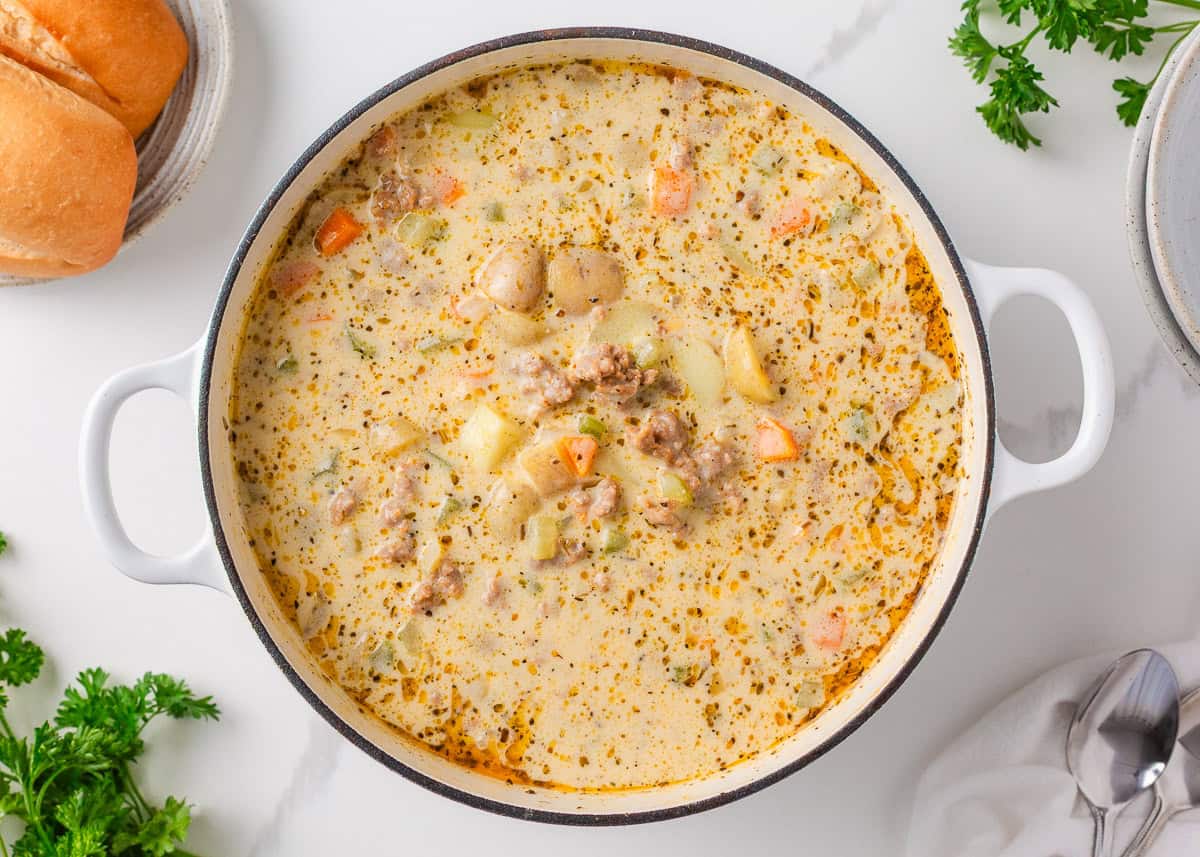 This creamy sausage potato soup is made in one pot with Italian sausage, tender potatoes, and a cheesy broth, it's a cozy way to satisfy the whole family! Finished creamy sausage and potato soup in Dutch oven with bread on the counter for serving.