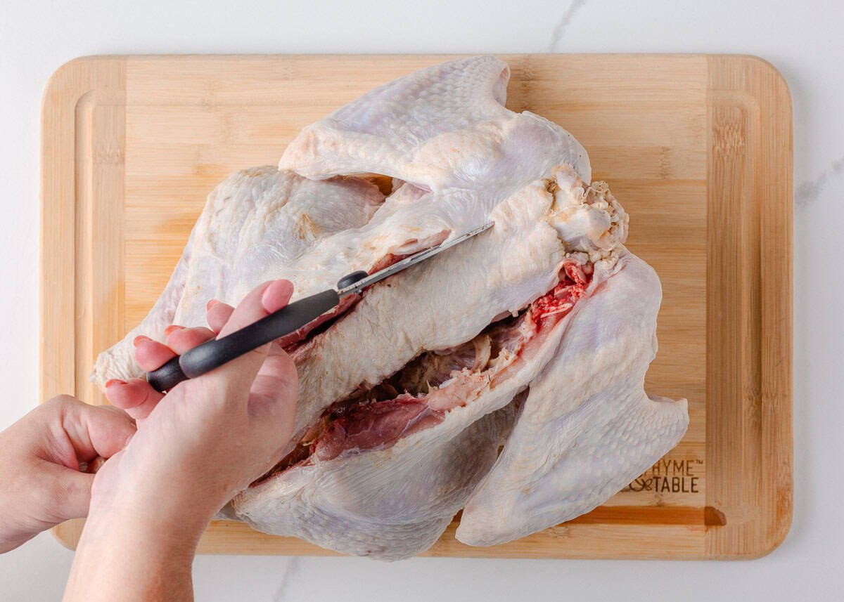 Cutting down the opposite side of the backbone with kitchen shears to remove it.