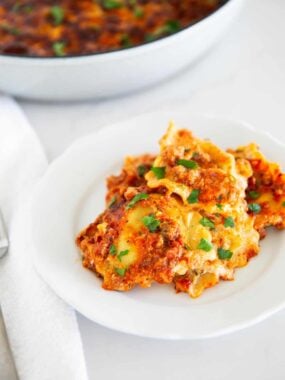 Million dollar ravioli casserole on a white plate garnish with parsley.