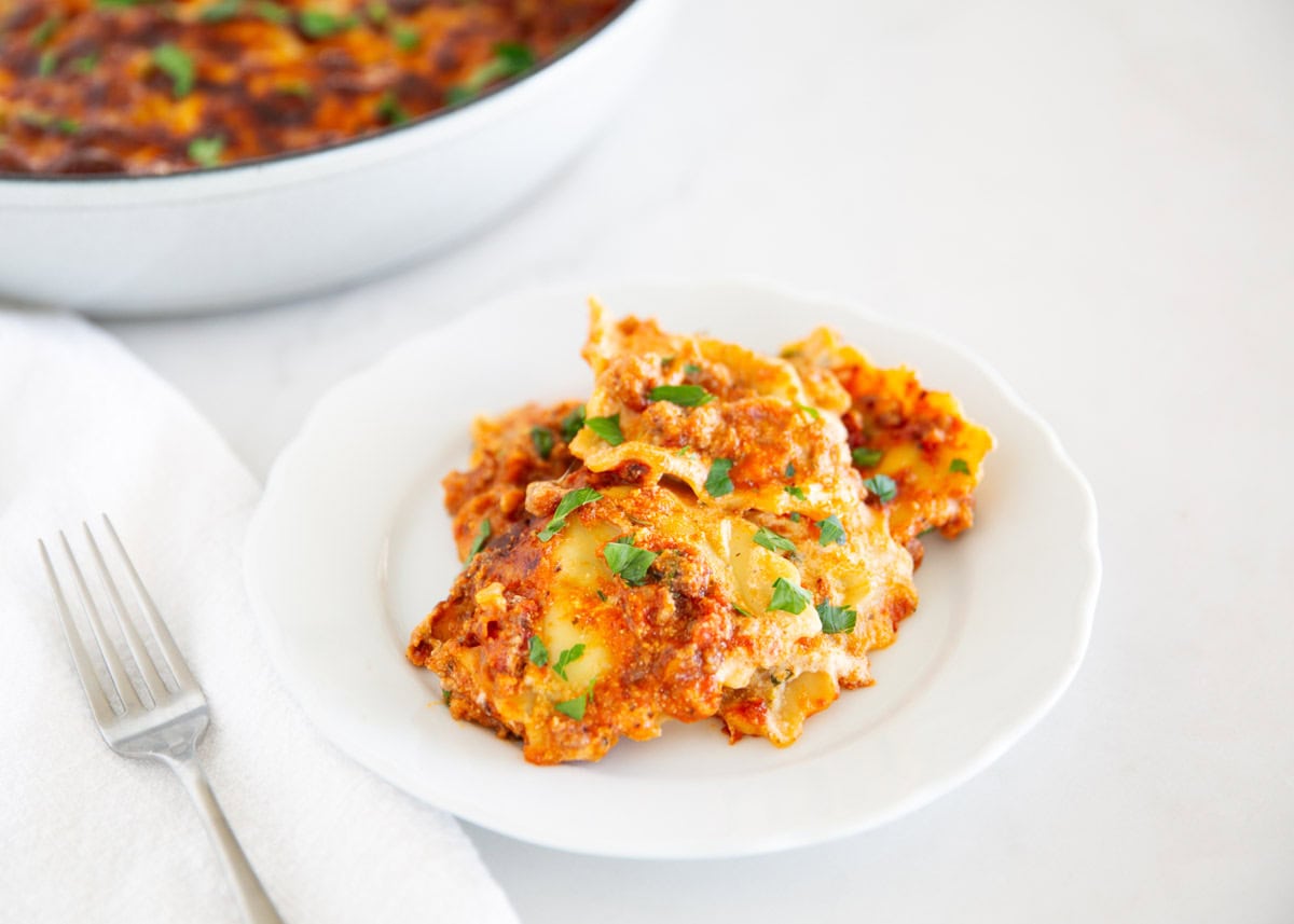A serving of million dollar ravioli casserole on a plate garnished with fresh parsley.