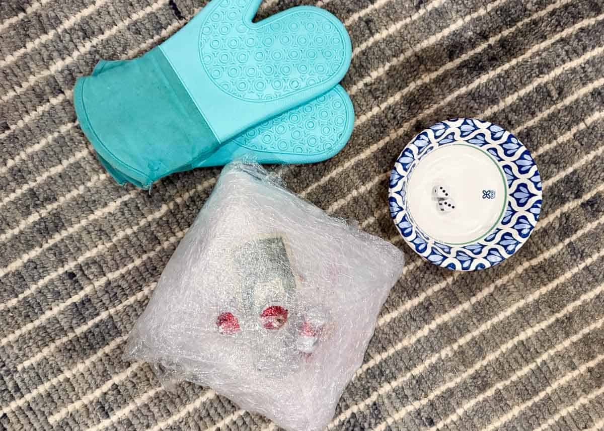 Showing essentials to play Saran wrap game including the Saran wrap ball, a bowl with two dice and oven mitts.