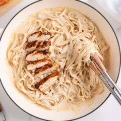 Creamy blackened chicken alfredo pasta in a white skillet with sliced chicken breast and grated parmesan on the side.