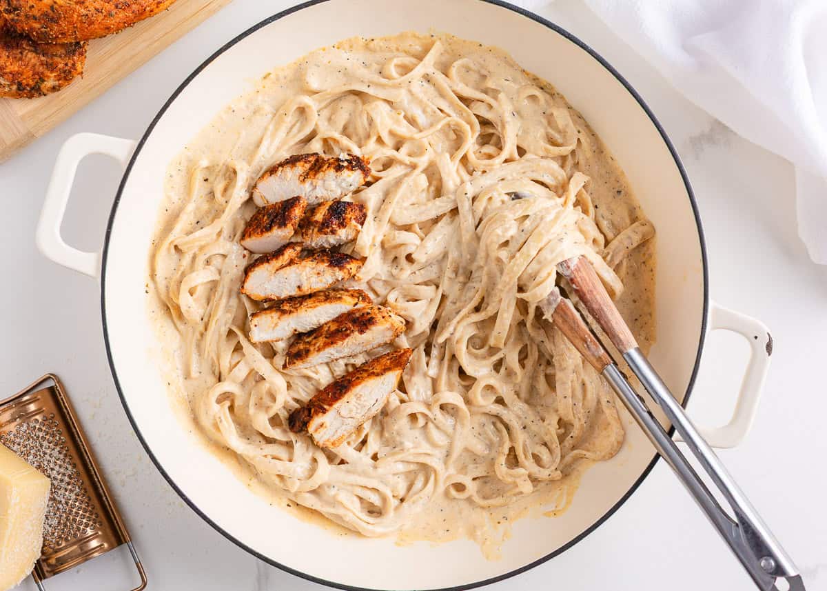 This blackened chicken Alfredo is an easy weeknight dinner that combines creamy Alfredo sauce with blackened chicken for a Southern twist on an Italian classic! Creamy blackened chicken alfredo pasta in a white skillet with sliced chicken breast and grated parmesan on the side.