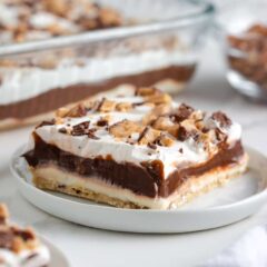 Piece of layered chocolate delight dessert on a white plate with chocolate pudding and whipped topping layers, topped with chopped toffee.
