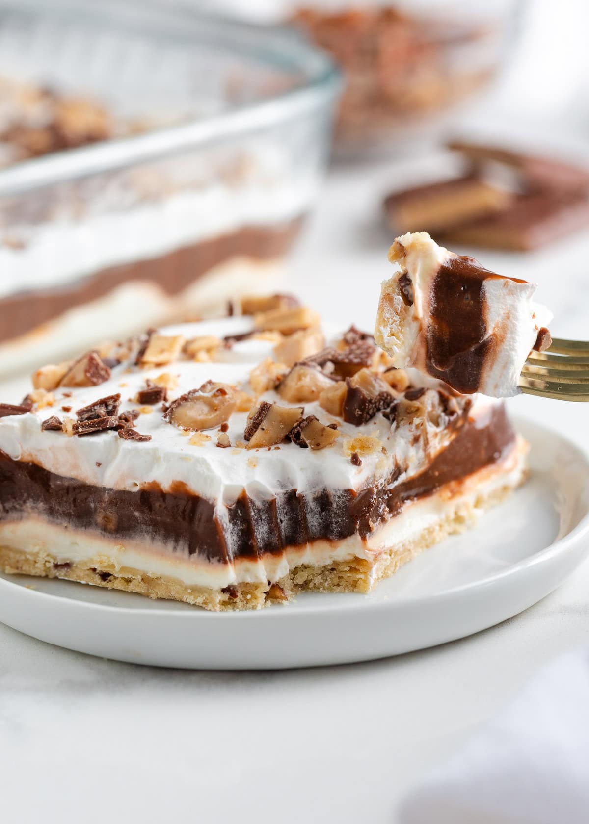 Close-up of creamy chocolate delight dessert with a forkful taken out showing layers of pudding, cream cheese, and whipped topping over a pecan crust.