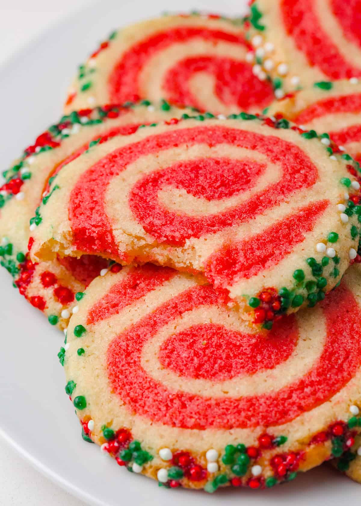Close up shot of a Christmas pinwheel cookie showing the soft texture, red swirl pattern, and colorful sprinkle edges.
