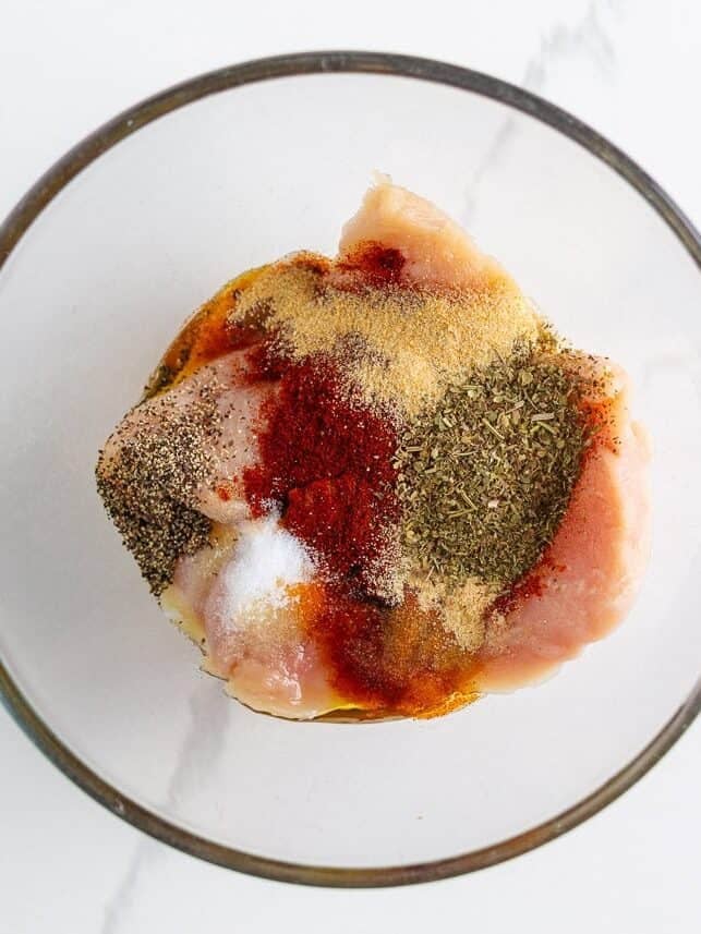 This blackened chicken Alfredo is an easy weeknight dinner that combines creamy Alfredo sauce with blackened chicken for a Southern twist on an Italian classic! Raw chicken breasts in a glass bowl topped with blackened seasoning mix including paprika, garlic powder, and Italian herbs.