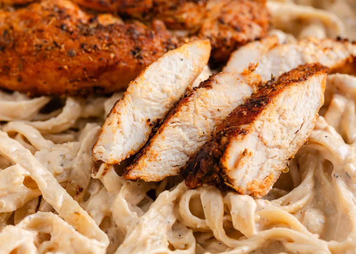 This blackened chicken Alfredo is an easy weeknight dinner that combines creamy Alfredo sauce with blackened chicken for a Southern twist on an Italian classic! Sliced blackened chicken served over creamy fettuccine Alfredo noodles.