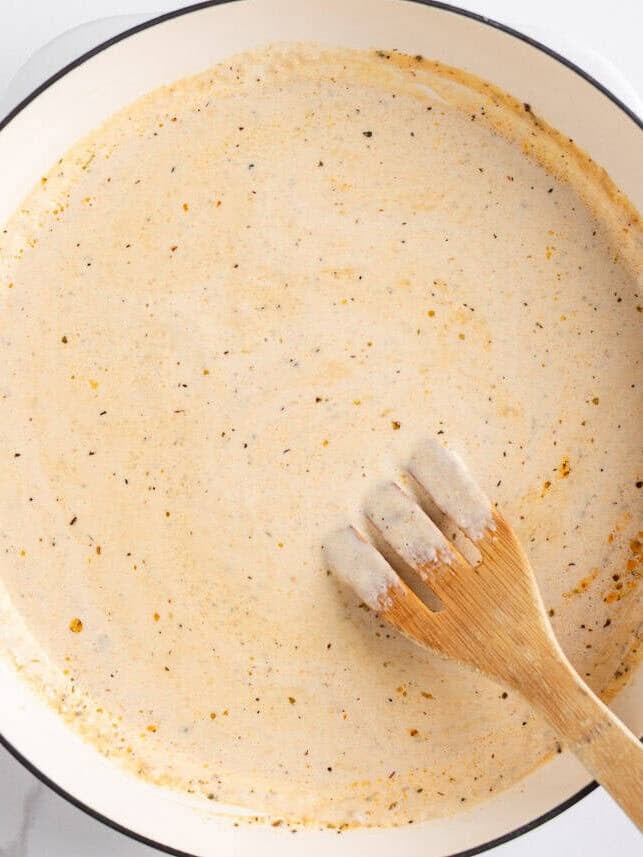 This blackened chicken Alfredo is an easy weeknight dinner that combines creamy Alfredo sauce with blackened chicken for a Southern twist on an Italian classic! Creamy homemade Alfredo sauce simmering in a white skillet with a wooden spatula stirring.