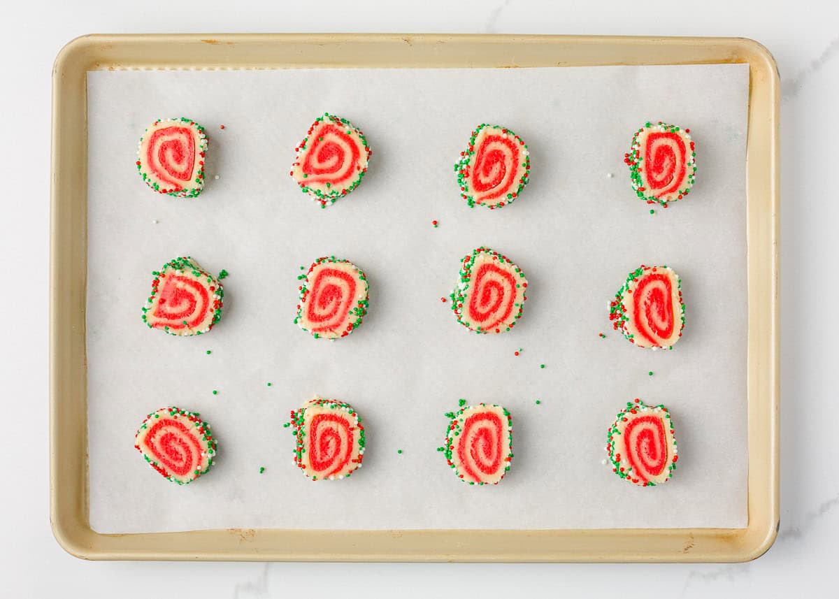 Unbaked Christmas pinwheel cookies arranged evenly on a parchment-lined baking sheet before baking.
