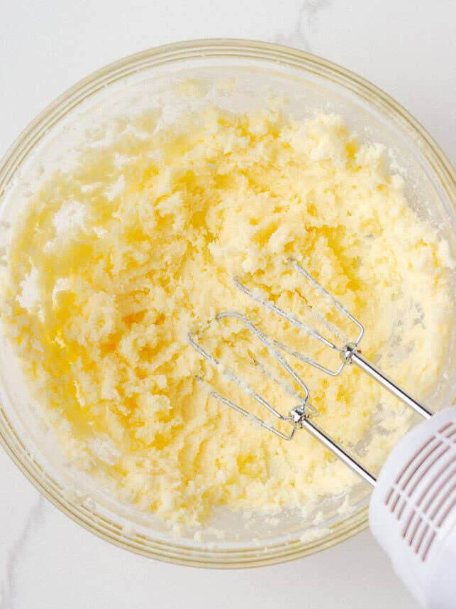Overhead view of a mixing bowl filled with creamed butter and sugar using a hand mixer to start the cookie dough.