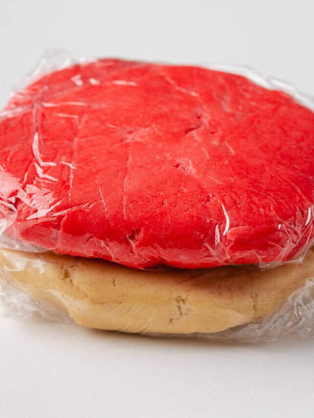 Red and plain cookie dough rounds wrapped in plastic wrap, stacked, and chilled before rolling out.