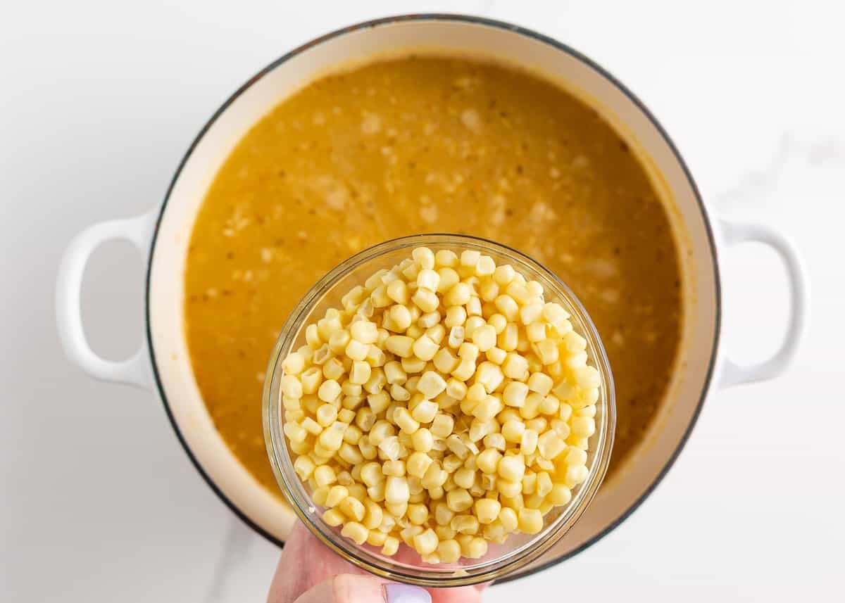 Adding frozen corn to a simmering pot of white chicken chili broth.