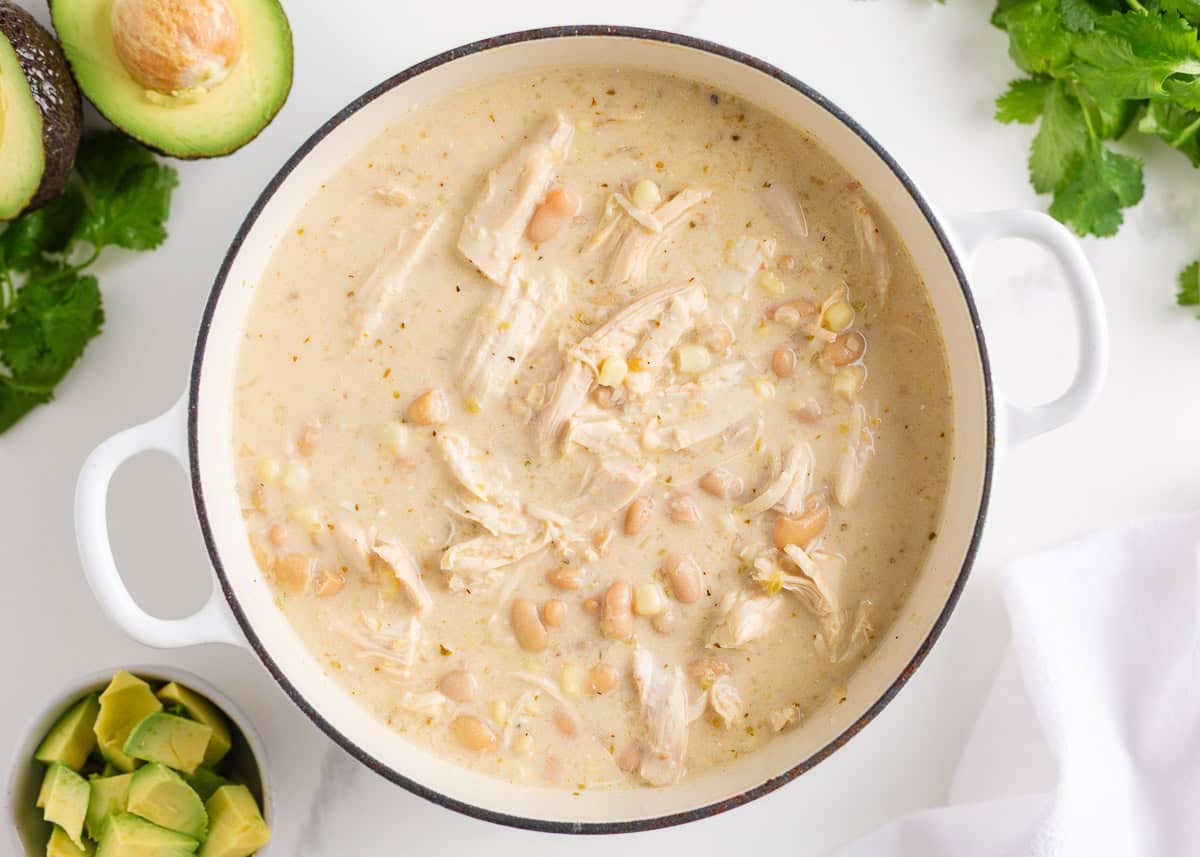 This white chicken chili is creamy, flavorful, and ready in just 30 minutes. Made with shredded chicken, white beans, and green chiles, it's great for game day or weeknights! Creamy white chicken chili simmering in a white Dutch oven, ready to serve.