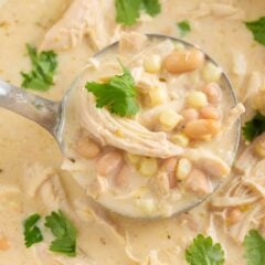Ladle scooping creamy white chicken chili with shredded chicken, corn, and beans from a white pot.