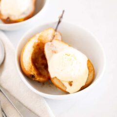 Two baked pear halves topped with vanilla ice cream in a serving bowl.