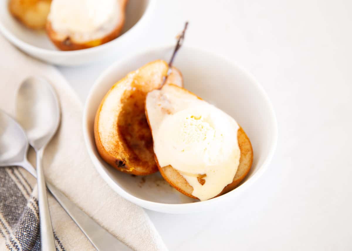Two warm baked pears served in small white bowls with vanilla ice cream.