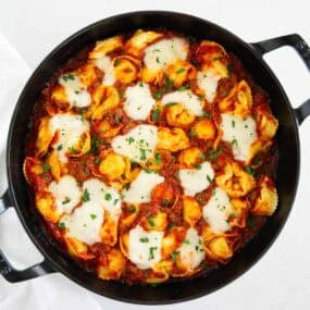 Freshly baked tortellini in a cast iron pan with melted mozzarella and herbs on top.