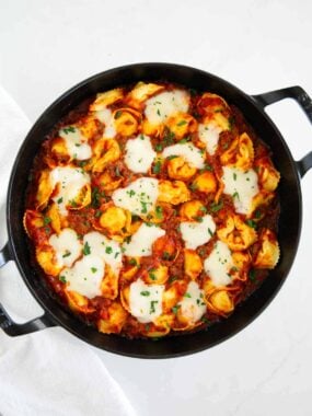 Freshly baked tortellini in a cast iron pan with melted mozzarella and herbs on top.