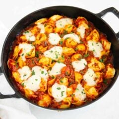 Baked tortellini in a cast iron skillet topped with melted mozzarella cheese and fresh parsley.