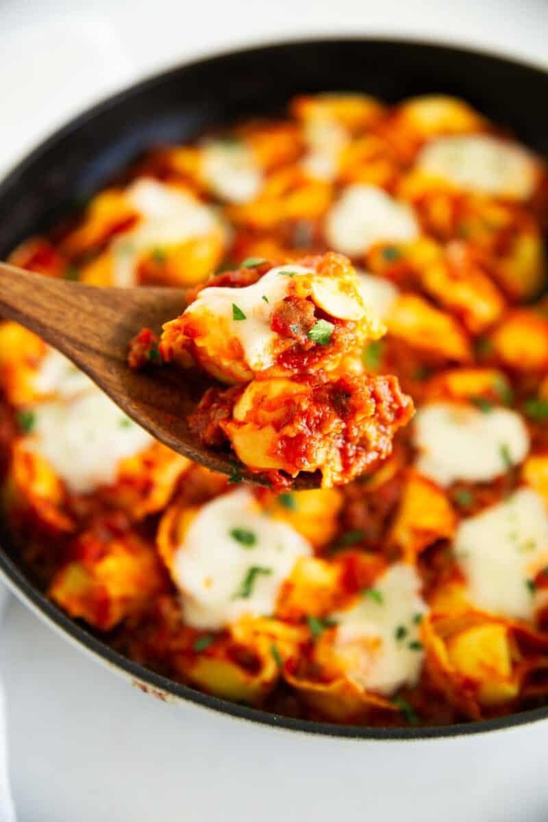 Spoonful of baked tortellini with sausage and melted mozzarella lifted from the skillet.