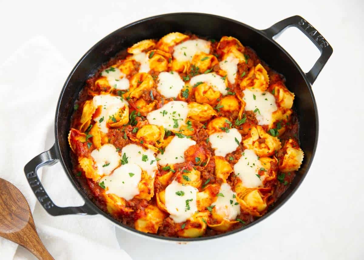 Baked tortellini in a cast iron skillet topped with melted mozzarella cheese and fresh parsley.