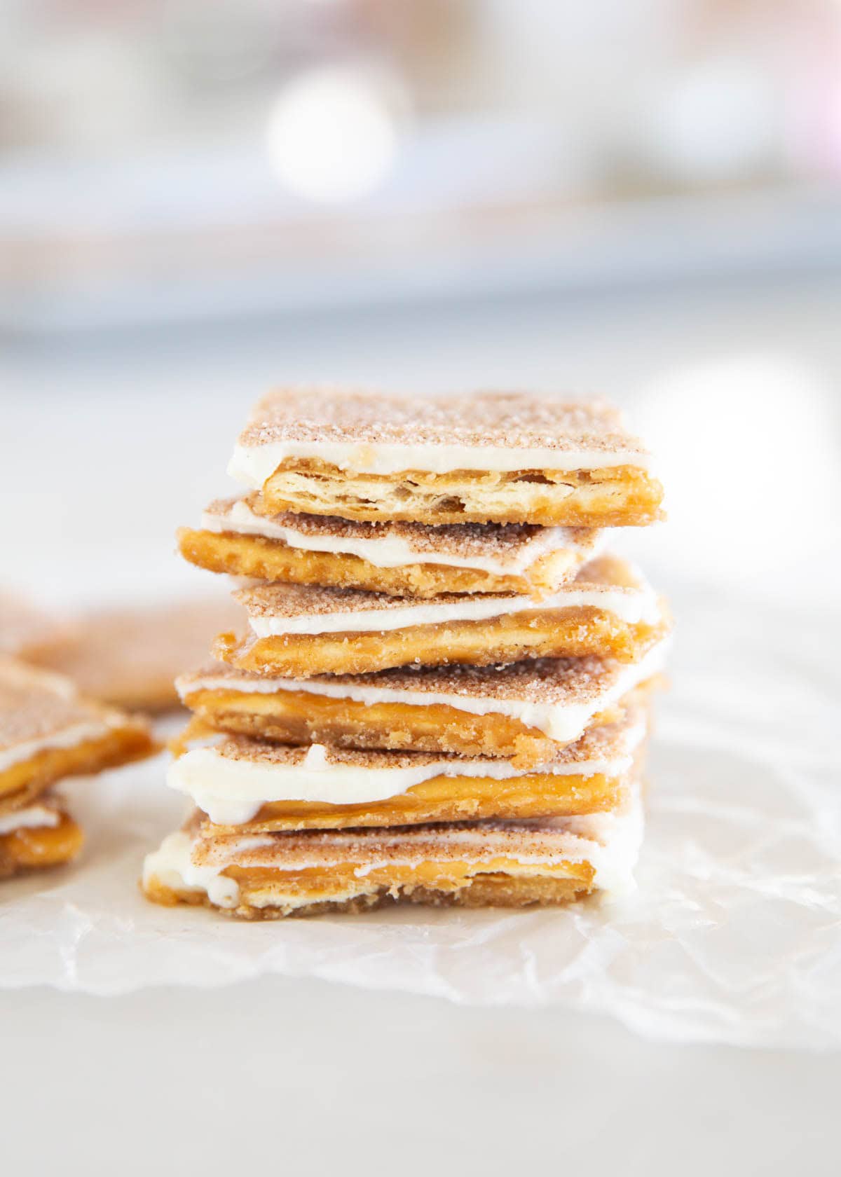 Churro-style saltine cracker toffee squares stacked on parchment, coated in white chocolate and cinnamon sugar.