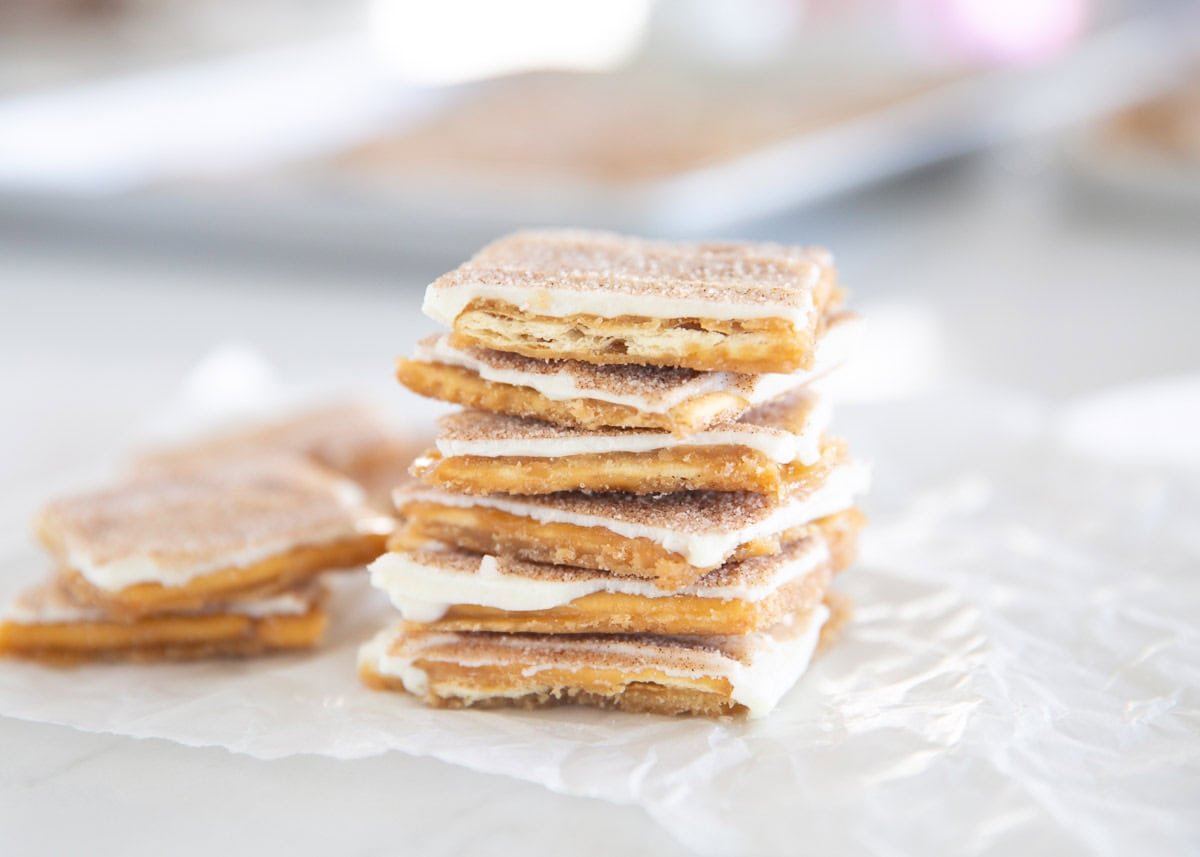 Churro saltine toffee pieces piled on parchment with more pieces in the background.