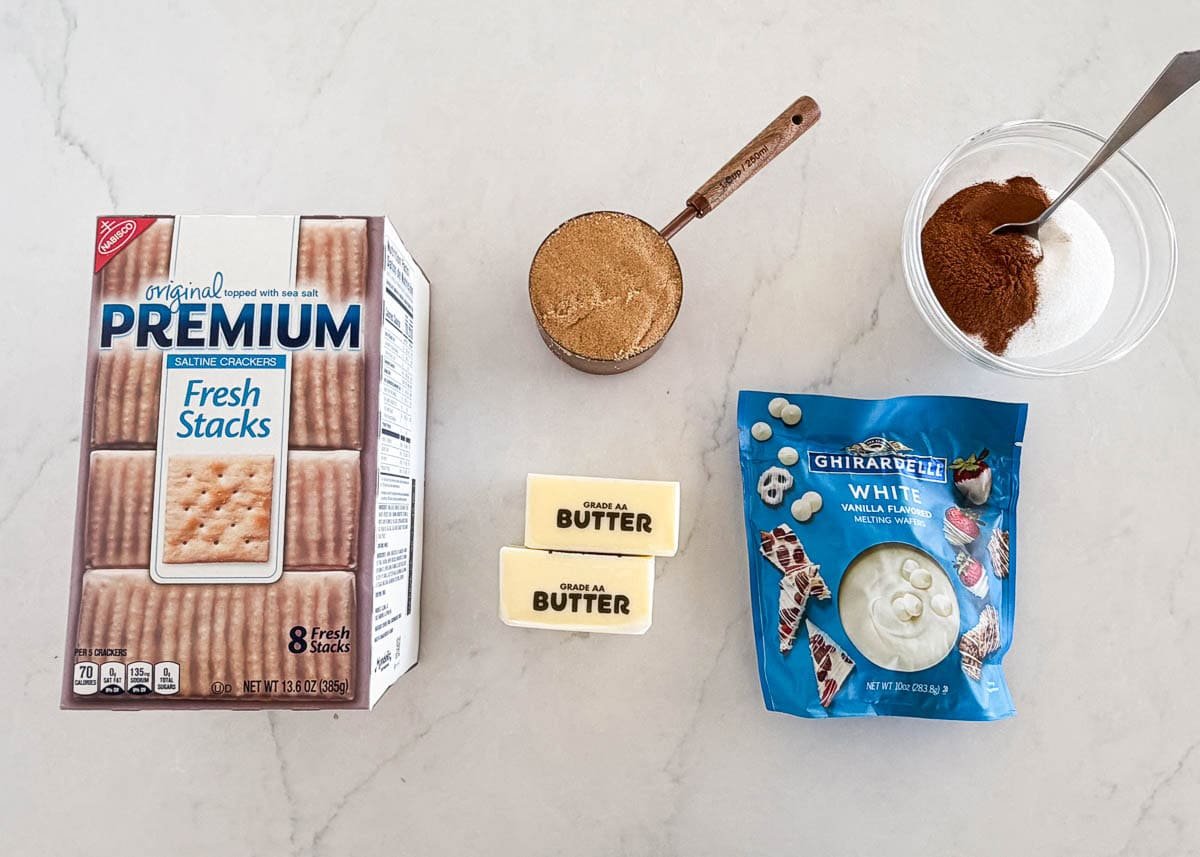 Ingredients for churro saltine toffee including saltine crackers, butter, brown sugar, white chocolate, cinnamon, and sugar.