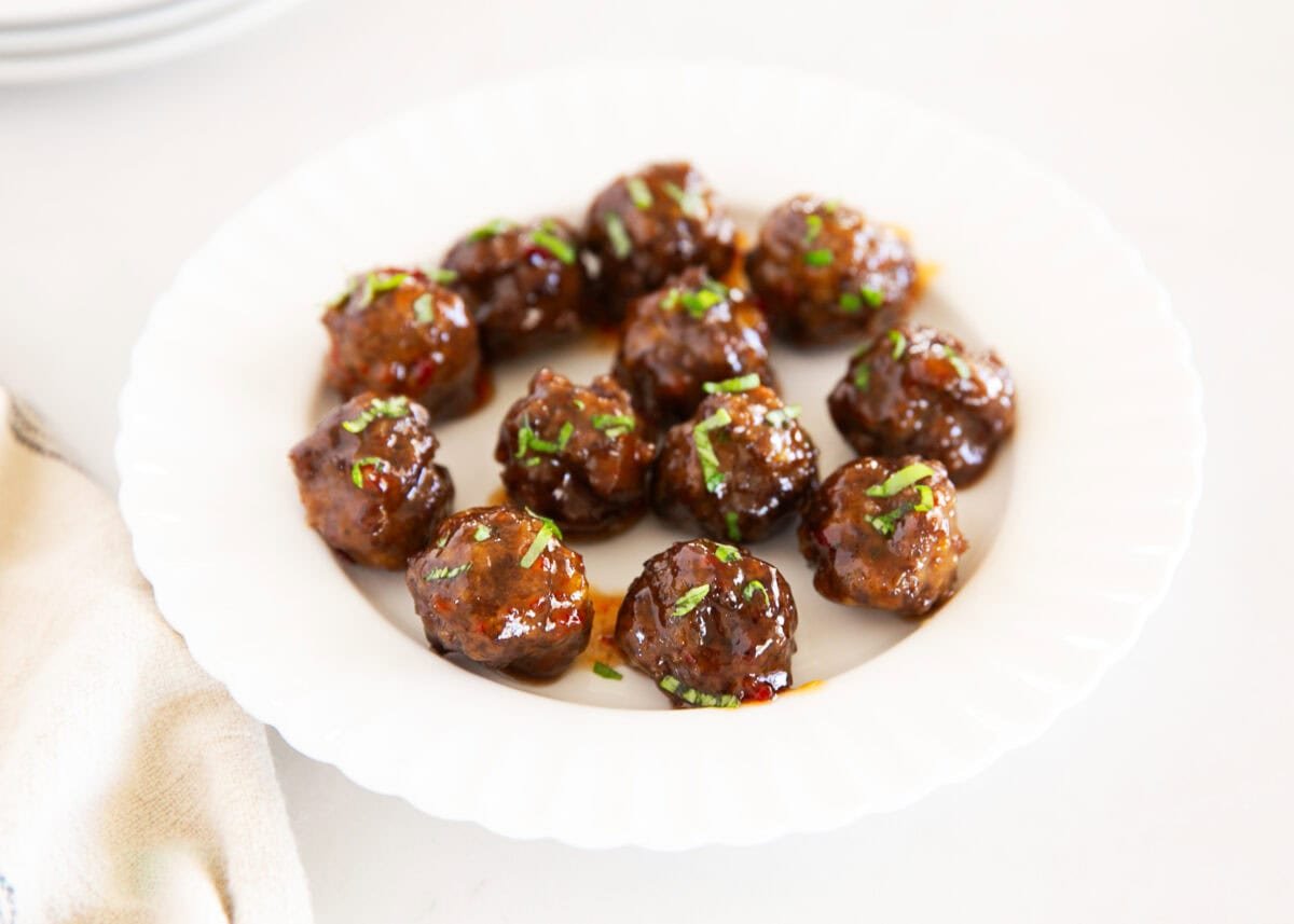 Plated cocktail meatballs coated in sweet chili sauce and sprinkled with fresh herbs on a white serving plate.