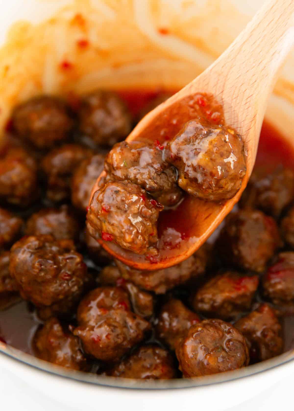 Freshly baked meatballs simmering in a sweet chili and brown sugar sauce in a white pot.