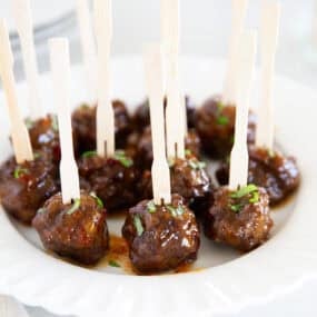 Close-up of glossy cocktail meatballs on skewers, topped with chopped herbs.