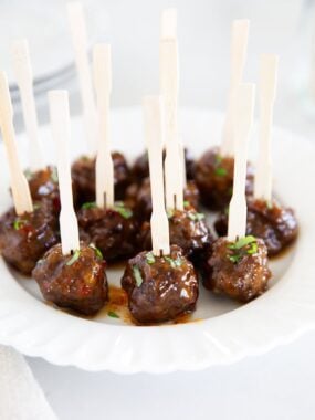 Close-up of glossy cocktail meatballs on skewers, topped with chopped herbs.