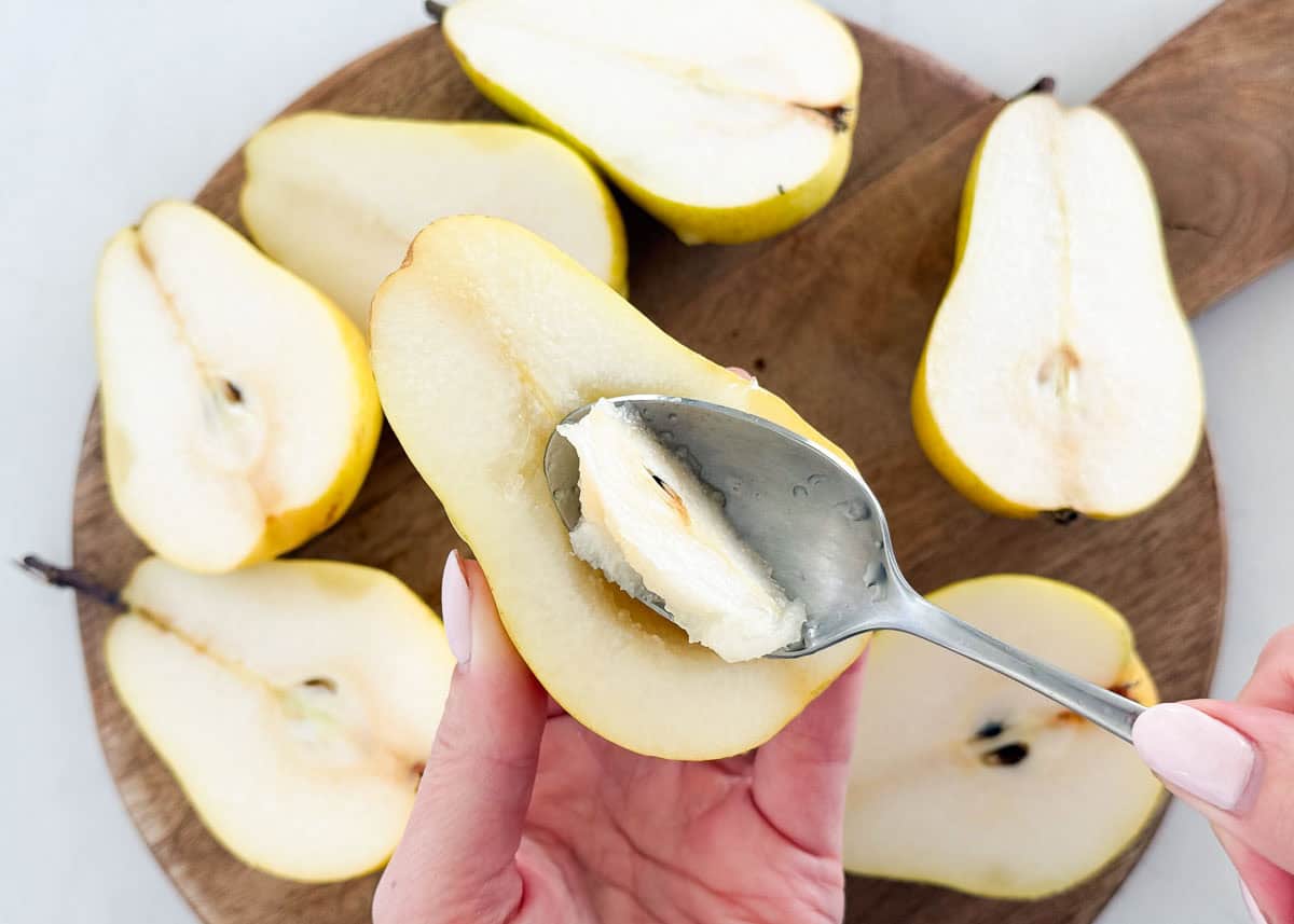 Using a spoon to remove the core from a pear half while prepping baked pears dessert.