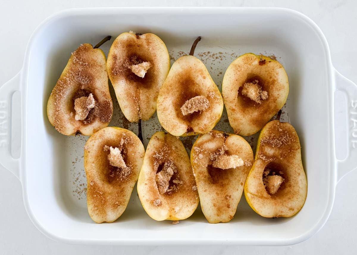 Halved pears topped with cinnamon brown sugar mixture before baking, showing how to make an easy baked pears recipe.