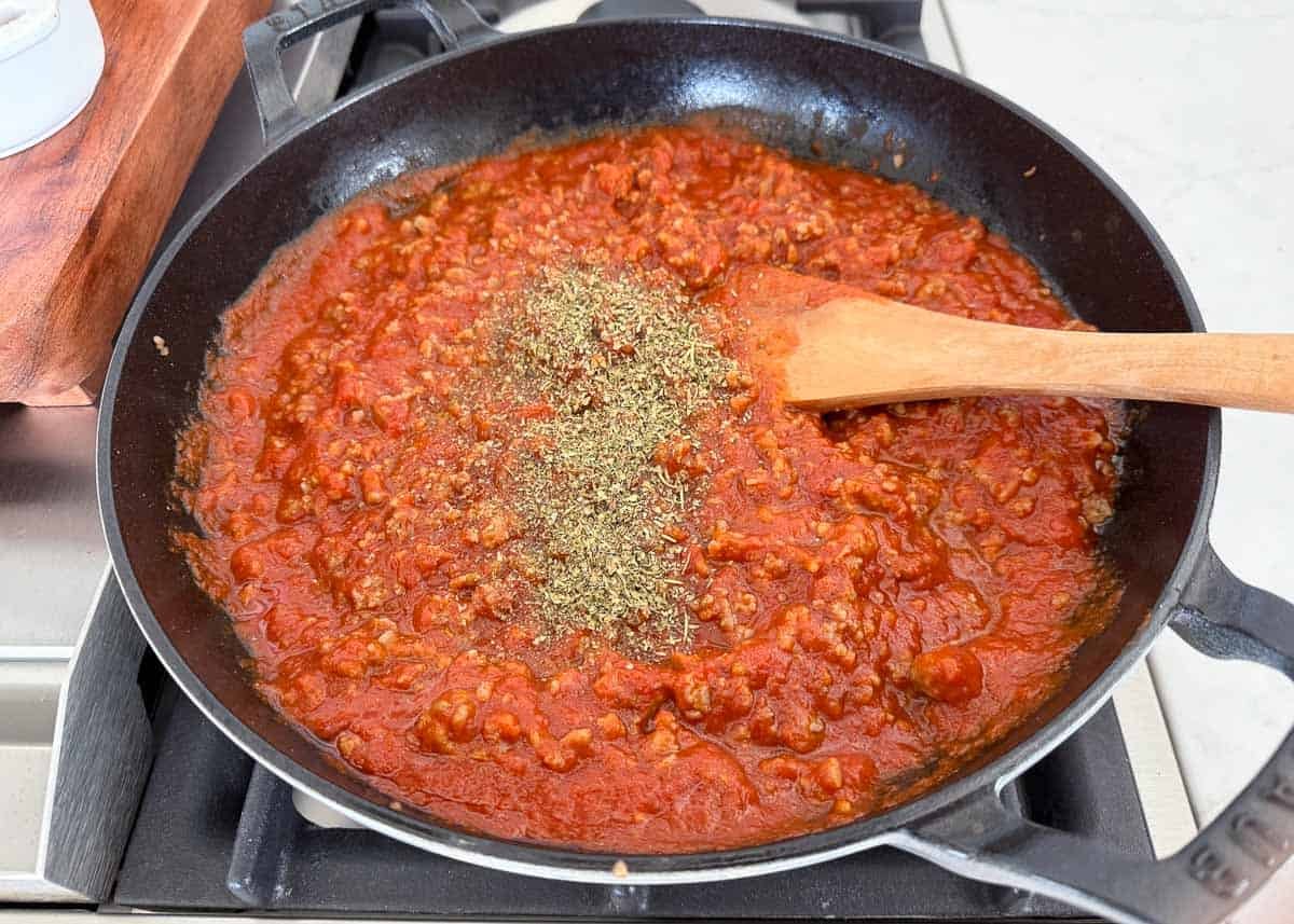 Adding marinara sauce to browned sausage in a skillet to make baked tortellini sauce.