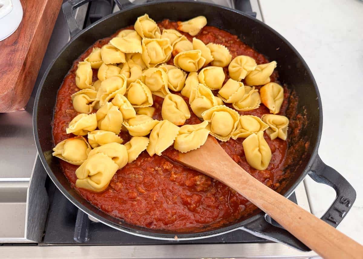 Mixing cheese tortellini into the sausage and marinara sauce in a skillet.