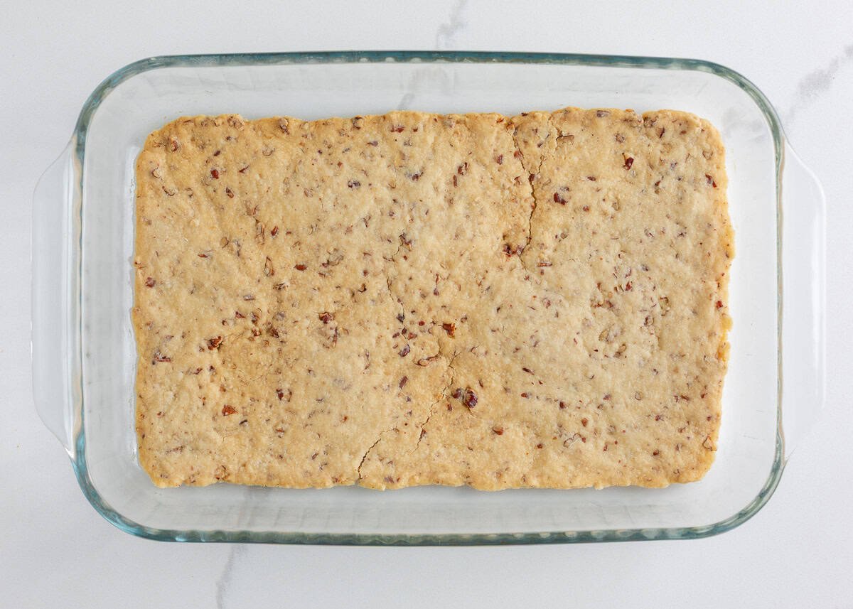 Baked pecan shortbread crust cooled in a glass baking dish, ready for the next layer.