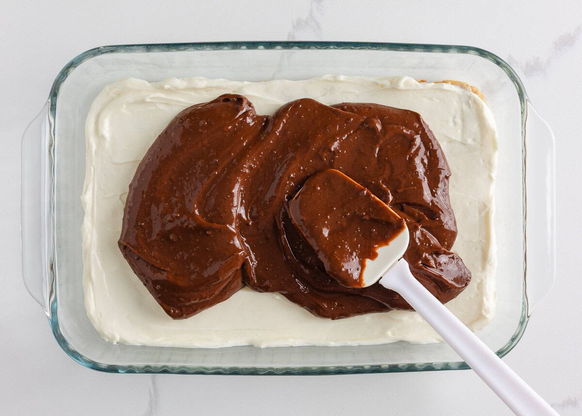 Layer of chocolate pudding being spread over the cream cheese layer with a spatula.